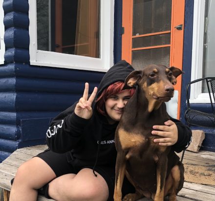 A student holds up a peace sign with one hand and has the other wrapped around his dog