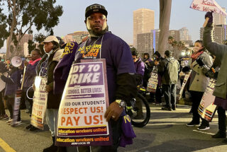 A man at the rally holding a sign that says "Ready to Strike. Respect Us! Pay Us!" 