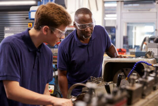 A young man and an older man work together on some machinery