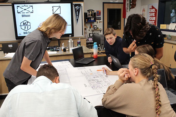 A group of students are gathered a table looking at blueprints