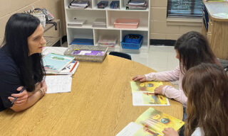 A teacher and two students work together at a small table in a classroom